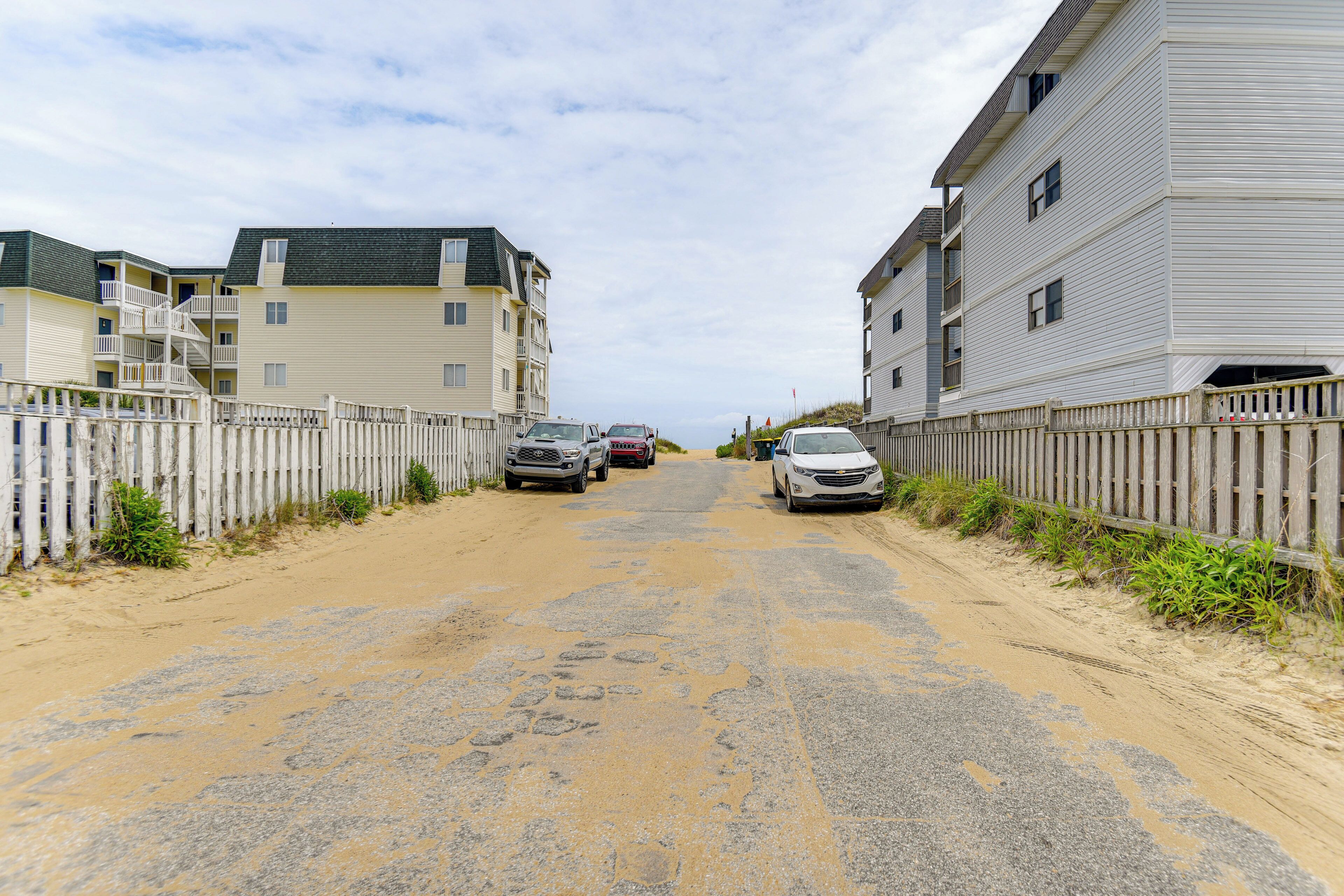 Un chemin de terre bordé de bâtiments à deux étages dotés de balcons, de voitures garées et d’une clôture en bois.