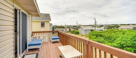 A wooden deck with a bench and a table, a sliding glass door, and a view of a green landscape.