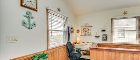 A room with wooden paneling, a desk with a chair, a potted plant, and nautical decor including an anchor and a ship.
