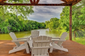 Eine Holzterrasse mit zwei Adirondack-Stühlen, die auf einen Fluss mit viel Grün blicken.