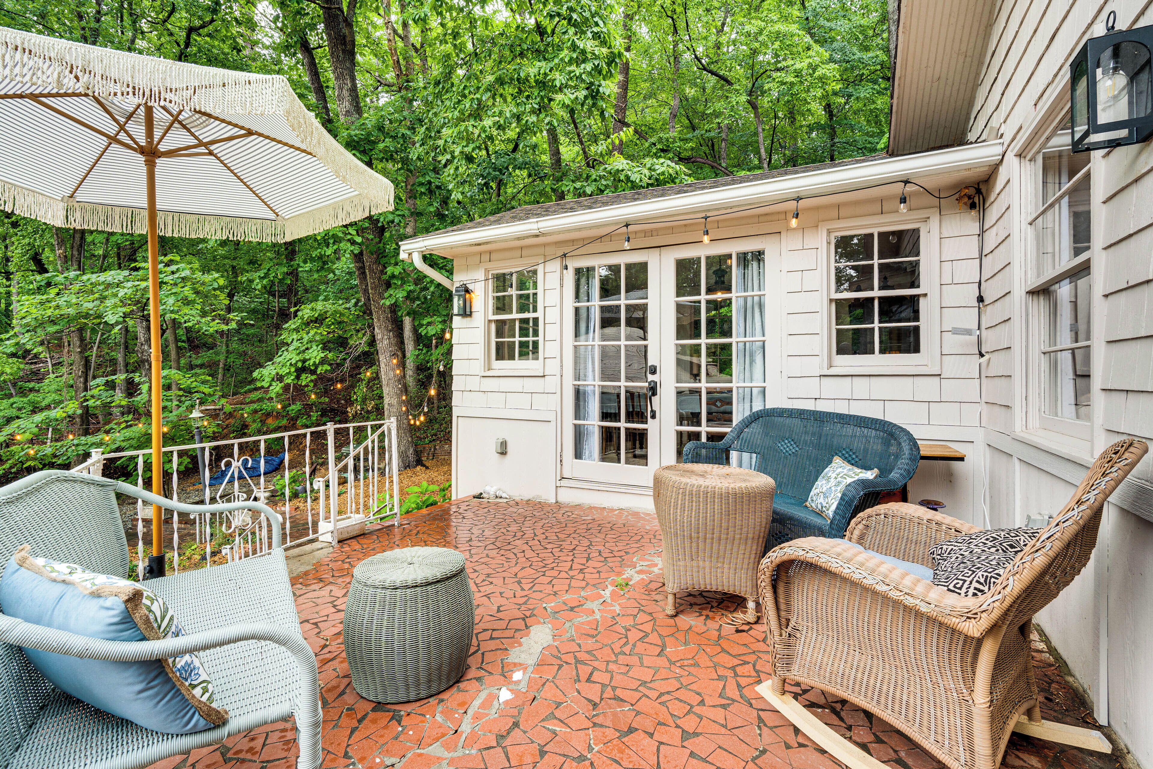 A covered patio with wicker furniture, a white umbrella, and a house with large windows.