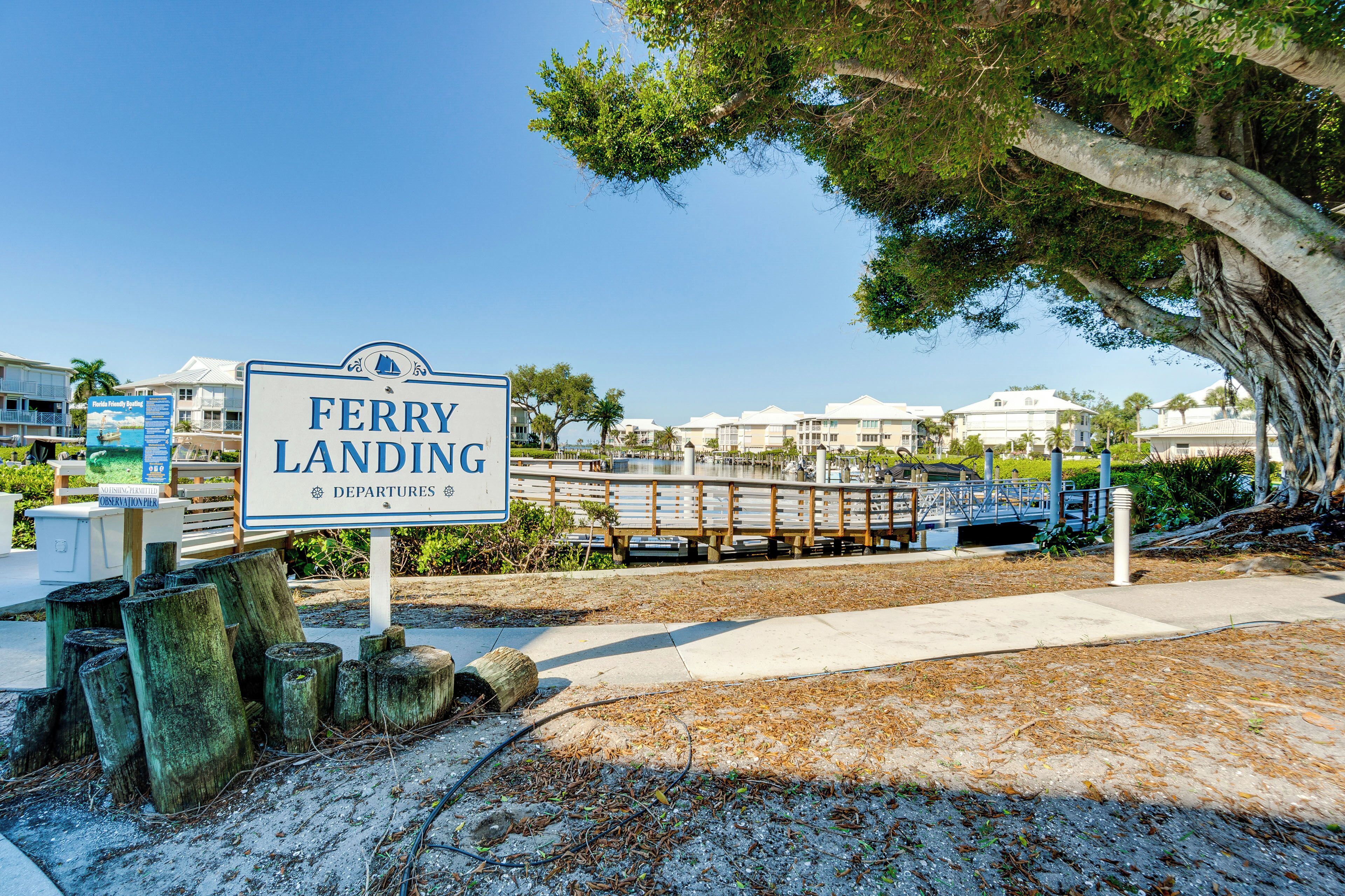 A sign for Ferry Landing with a view of a bridge and buildings in the background.