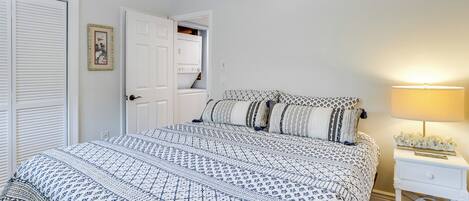 A bedroom with a bed, a nightstand, a lamp, a wardrobe, and a door leading to another room.