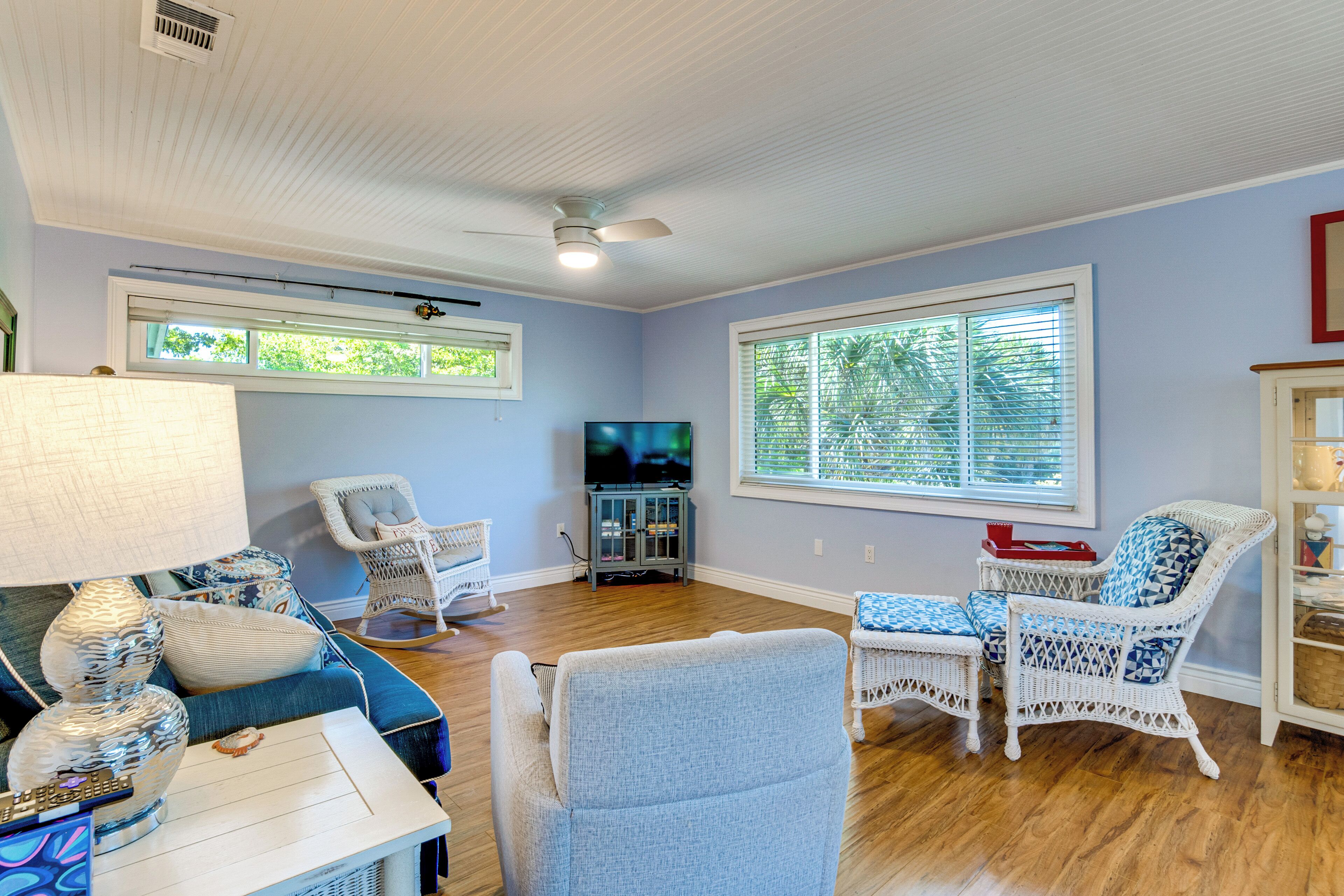 A living room with a blue sofa, wicker chairs, a TV stand, and a ceiling fan.