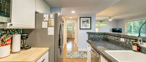 A modern kitchen with a refrigerator, microwave, and stove, a wooden countertop, and a tiled backsplash.
