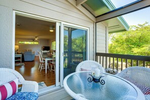 Une terrasse couverte, aménagée avec des meubles en osier, une table en verre et une porte-fenêtre coulissante donnant sur un espace de salle à manger intérieur.