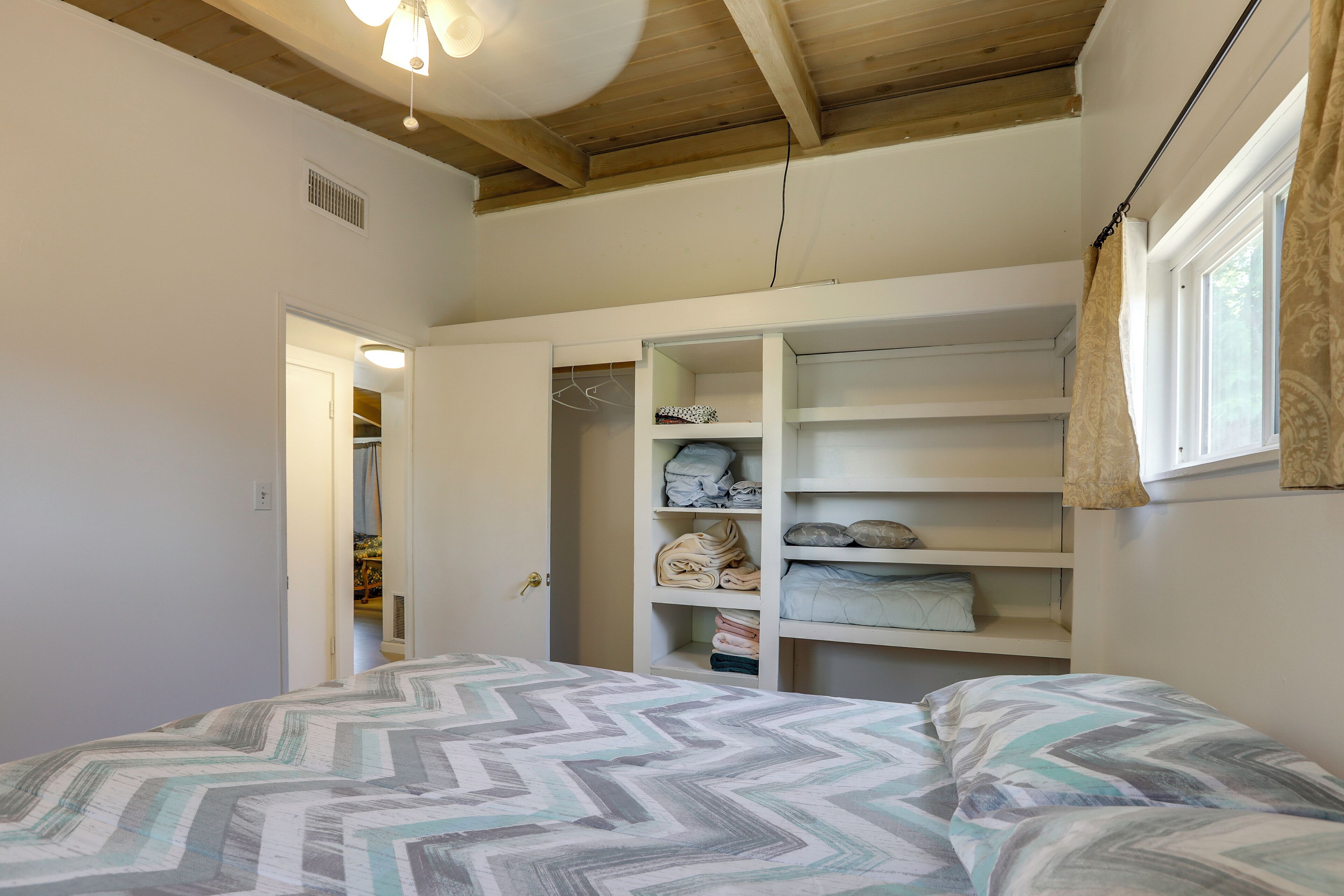 A bedroom with a bed, a closet with shelves, and a window with curtains.