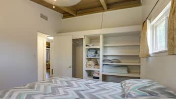 A bedroom with a bed, a closet with shelves, and a window with curtains.
