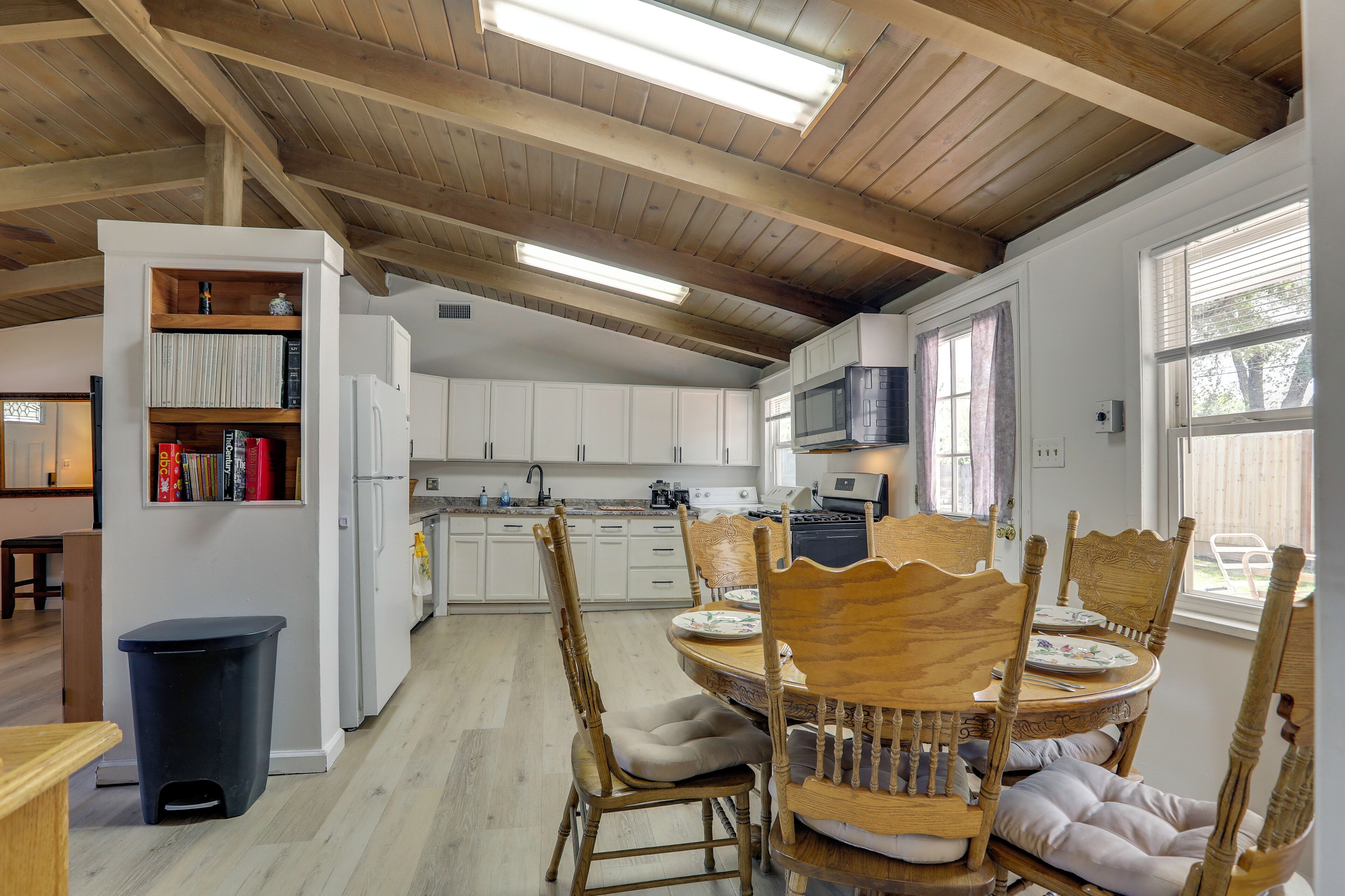 A kitchen with wooden beams, white cabinets, a dining table with chairs, and a trash bin.