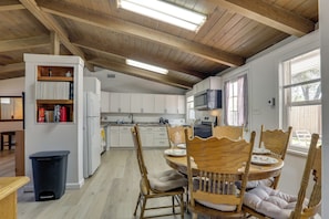 A kitchen with wooden beams, white cabinets, a dining table with chairs, and a trash bin. - 1950s Home Quiet Street Near Dtwn 1 Mi to Marina (Sparks)