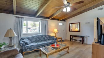 A living room with a sofa, a coffee table, a ceiling fan, a lamp, a bench, and a television.