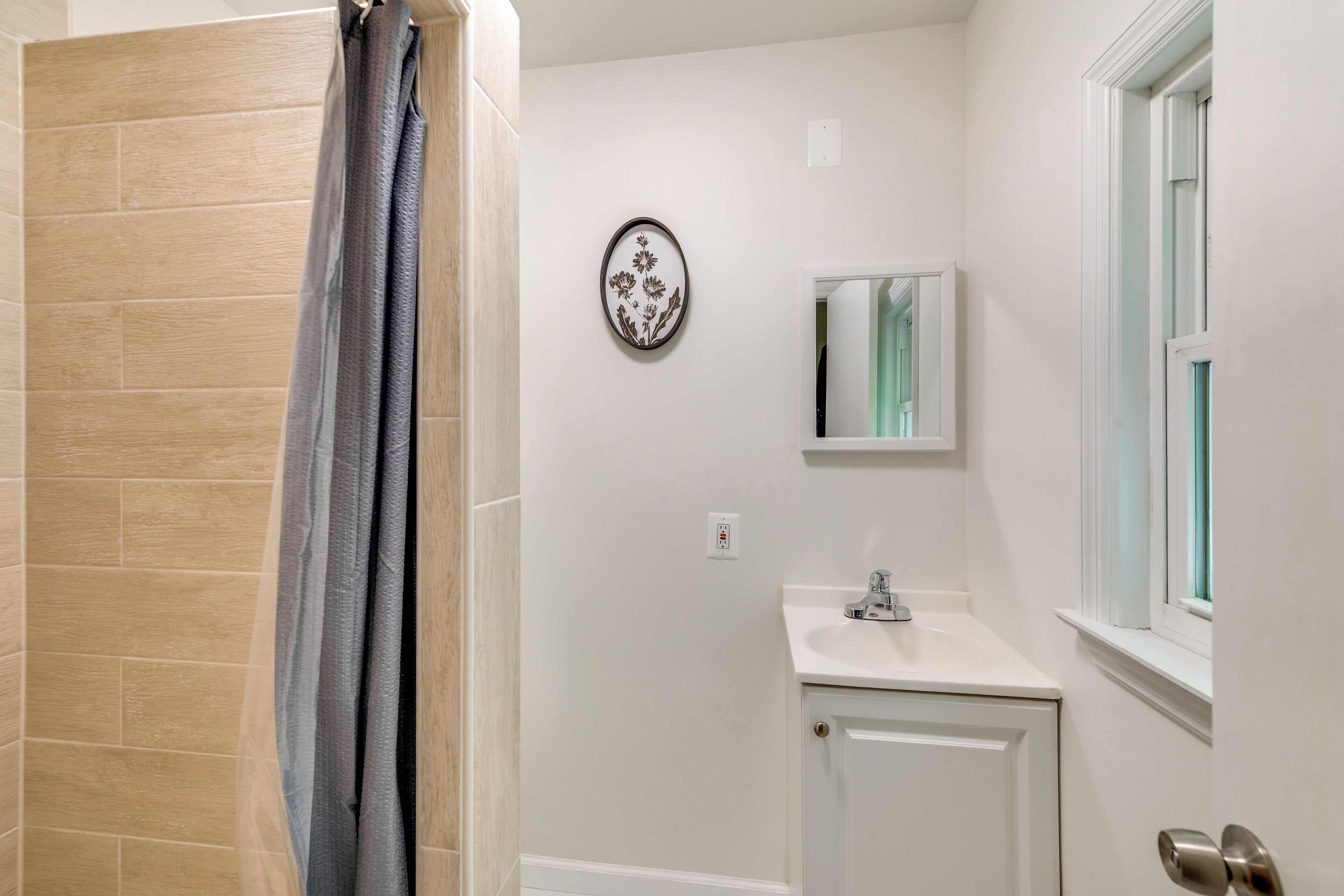 A bathroom with a shower, a sink, a mirror, and a window.