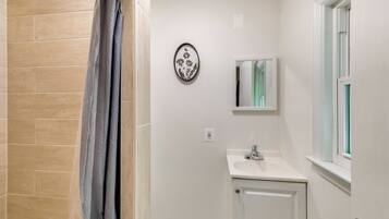 A bathroom with a shower, a sink, a mirror, and a window.