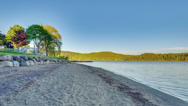 A beach with a stone wall, trees, and a calm lake. - Easy Schroon Lake Living! Close to Marina & Town (Schroon Lake)
