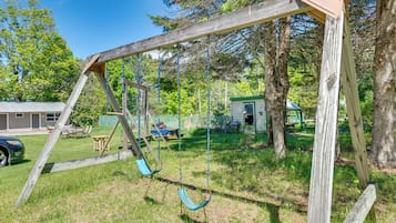 Ein hölzernes Schaukelgestell in einem Garten mit Haus, Bäumen und Rasen.