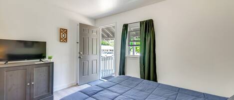 A bedroom with a bed, a TV on a cabinet, a door leading outside, and a window with curtains.