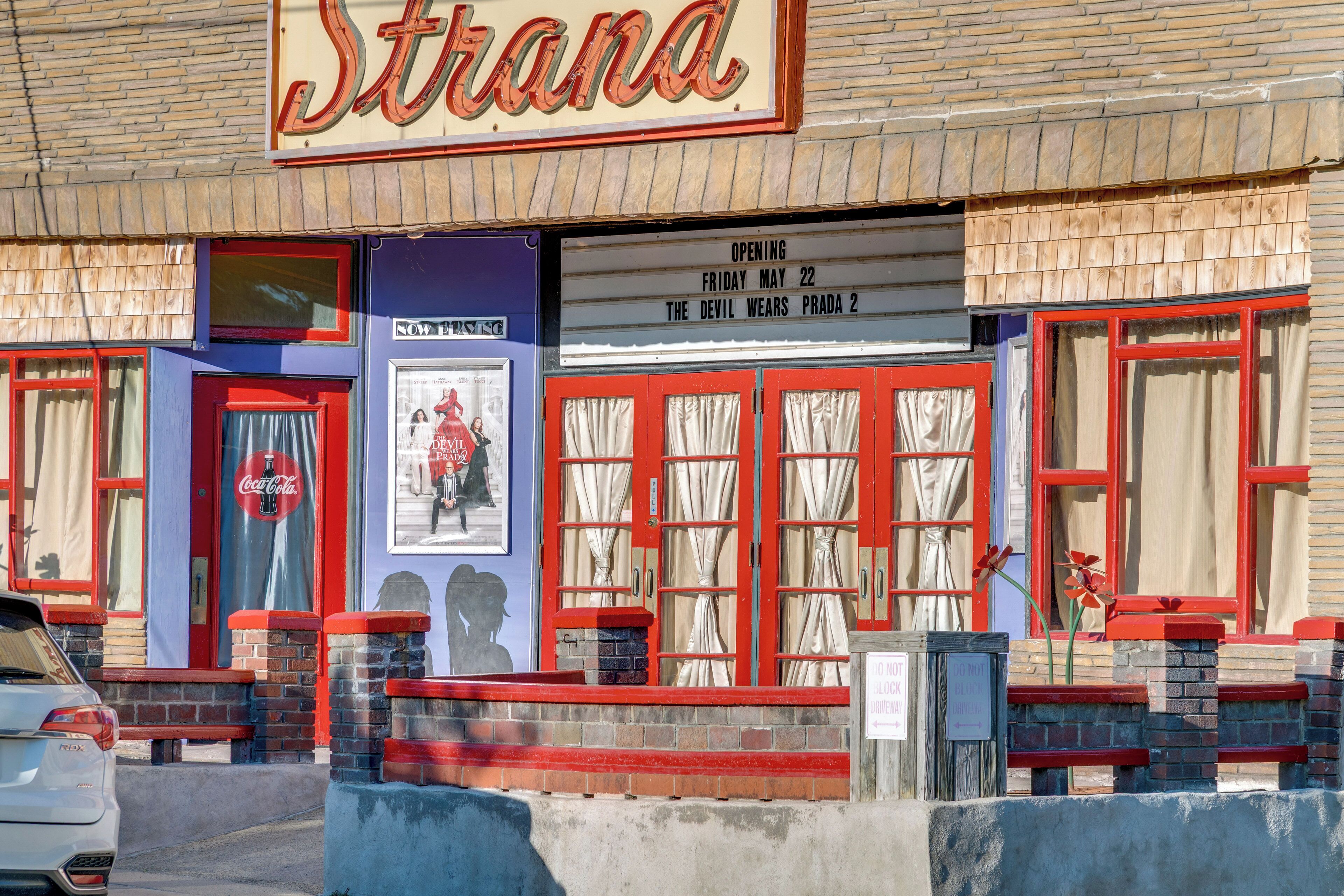 Ein Theater mit einer Laufstegwerbeanlage, auf der 'Strana' steht, einem Coca-Cola-Schild und einem Plakat für 'The Devil Wears Prada 2'.