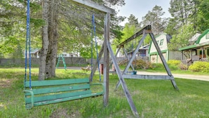 A wooden swing set and a bench in a grassy area with a house in the background.