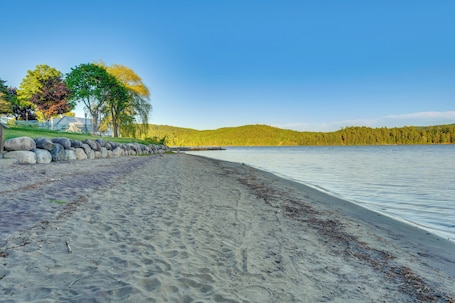 A sandy beach with a stone wall, trees, and a clear view of a lake.. Schroon Lake Room < 1 Mi to Marina & Beach!