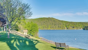 A park with a bench by a lake, a wooden walkway, and a hill in the background.