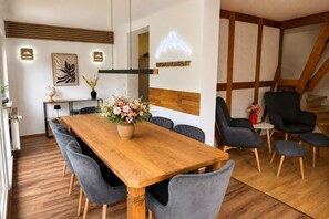 A dining area with a wooden table, grey upholstered chairs, a vase with flowers, and a staircase with wooden beams. - Apartment Blankenburg Harz, BERGMOMENT 8 persons, old town, balcony, fireplace, parking lot (Blankenburg (Harz))