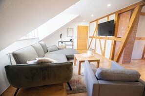 A loft-style living room with a sectional sofa, a small table, and a TV mounted on a wooden beam. - Apartment Blankenburg Harz, BERGMOMENT 8 persons, old town, balcony, fireplace, parking lot (Blankenburg (Harz))