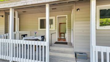 A covered porch with a white railing, a table with chairs, and a small step leading to a door.