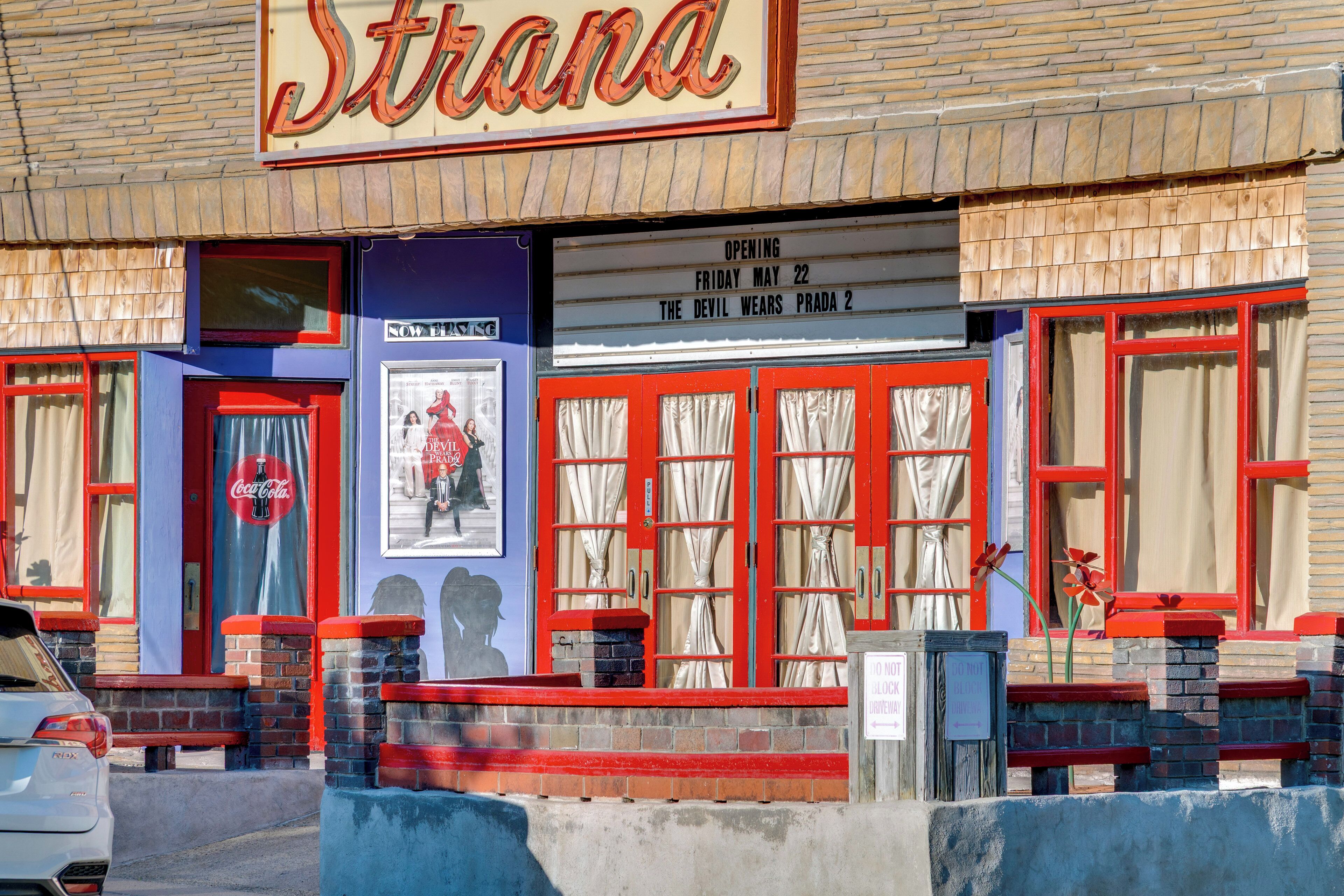 Un bâtiment orné d’une enseigne lumineuse indiquant « Strana », d’une enseigne Coca-Cola et d’une affiche pour le film « Le Diable s’habille en Prada 2 ».
