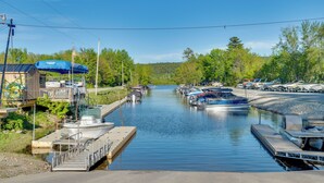 A marina with boats docked, a small building with a blue awning, and a dock extending into the water. - Cozy Room Near Schroon Lake Marina, Town & Beach! (Schroon Lake)