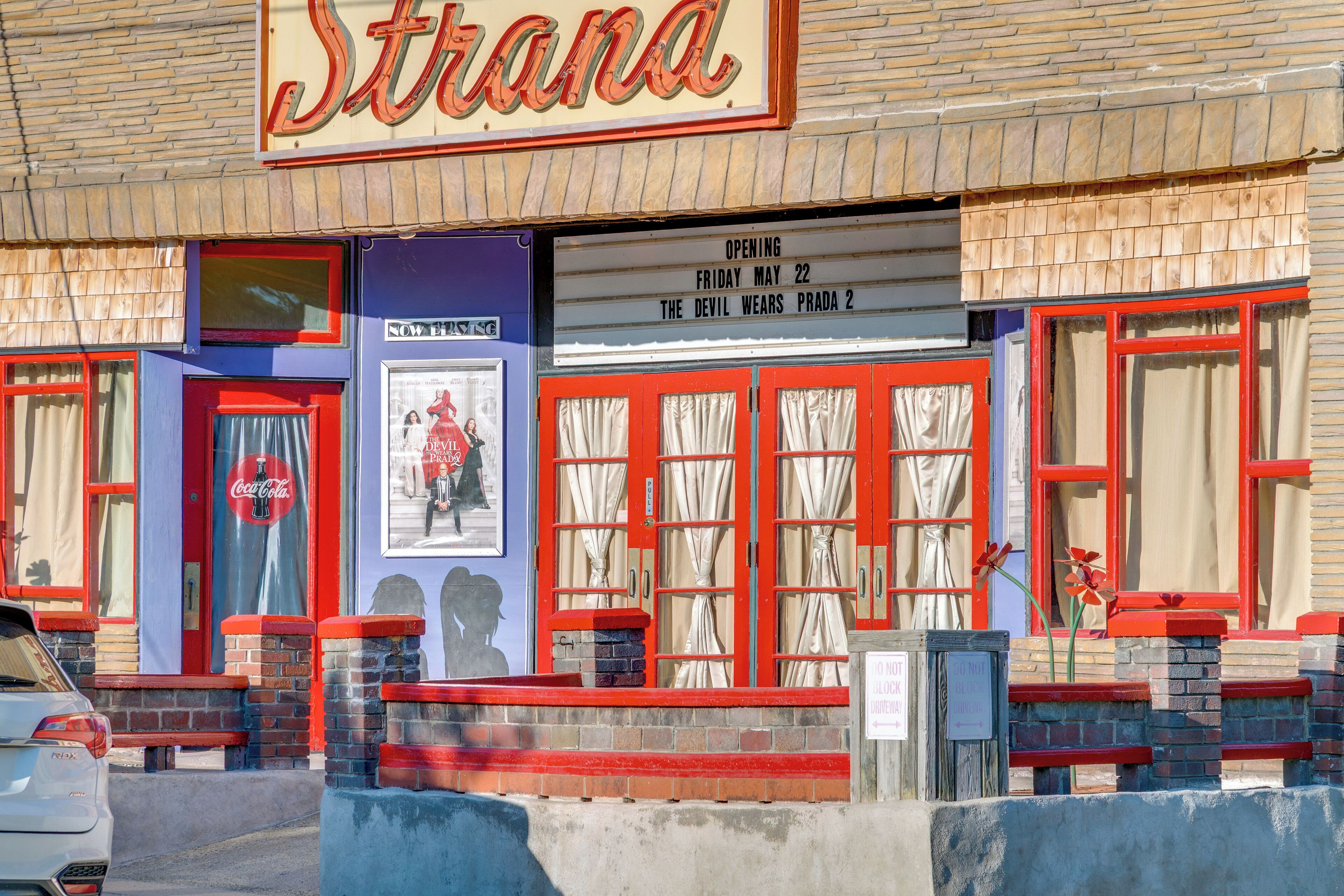 Un bâtiment orné d’une enseigne lumineuse indiquant « Strana », d’une enseigne Coca-Cola et d’une autre faisant la promotion du film « Le Diable s’habille en Prada 2 », dont la sortie est prévue le vendredi 22 mai.