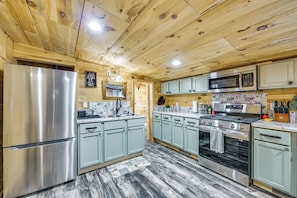 A kitchen with wooden ceiling, stainless steel appliances, and light green cabinets.
