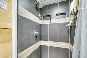 A shower with a handheld showerhead, a wall-mounted towel rack, and a small shelf.