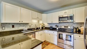 A modern kitchen with white cabinets, a granite countertop, stainless steel appliances, and a tiled backsplash. - Sunroom & Deck! Golf Retreat in Keowee Key (Salem)