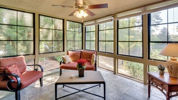 A sunlit room with a ceiling fan, a sofa, a coffee table, and large windows offering a view of trees. - Sunroom & Deck! Golf Retreat in Keowee Key (Salem)
