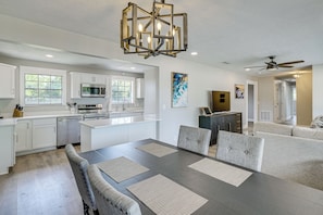 Une cuisine moderne avec des meubles blancs, un coin repas dotĂ© dâune table en bois foncĂ© et de chaises Ă revĂȘtement gris, ainsi quâun ventilateur de plafond.