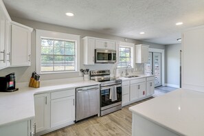 A modern kitchen with white cabinetry, stainless steel appliances, and large windows.