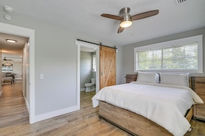 Une chambre Ă coucher avec un lit, un plancher en bois, un ventilateur de plafond et une fenĂȘtre avec des stores.