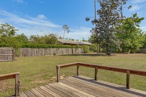 A wooden deck with a railing, a grassy yard, a wooden fence, and a building with a metal roof.