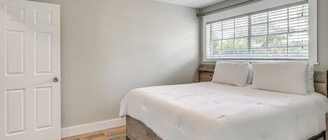 A bedroom with a bed, a ceiling fan, a window with blinds, and a door.