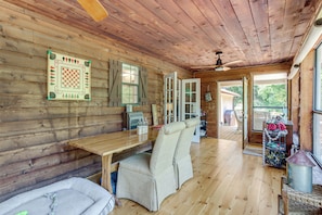 Interior de una cabaña de madera con una mesa, un banco acolchado y una ventana con contraventanas.