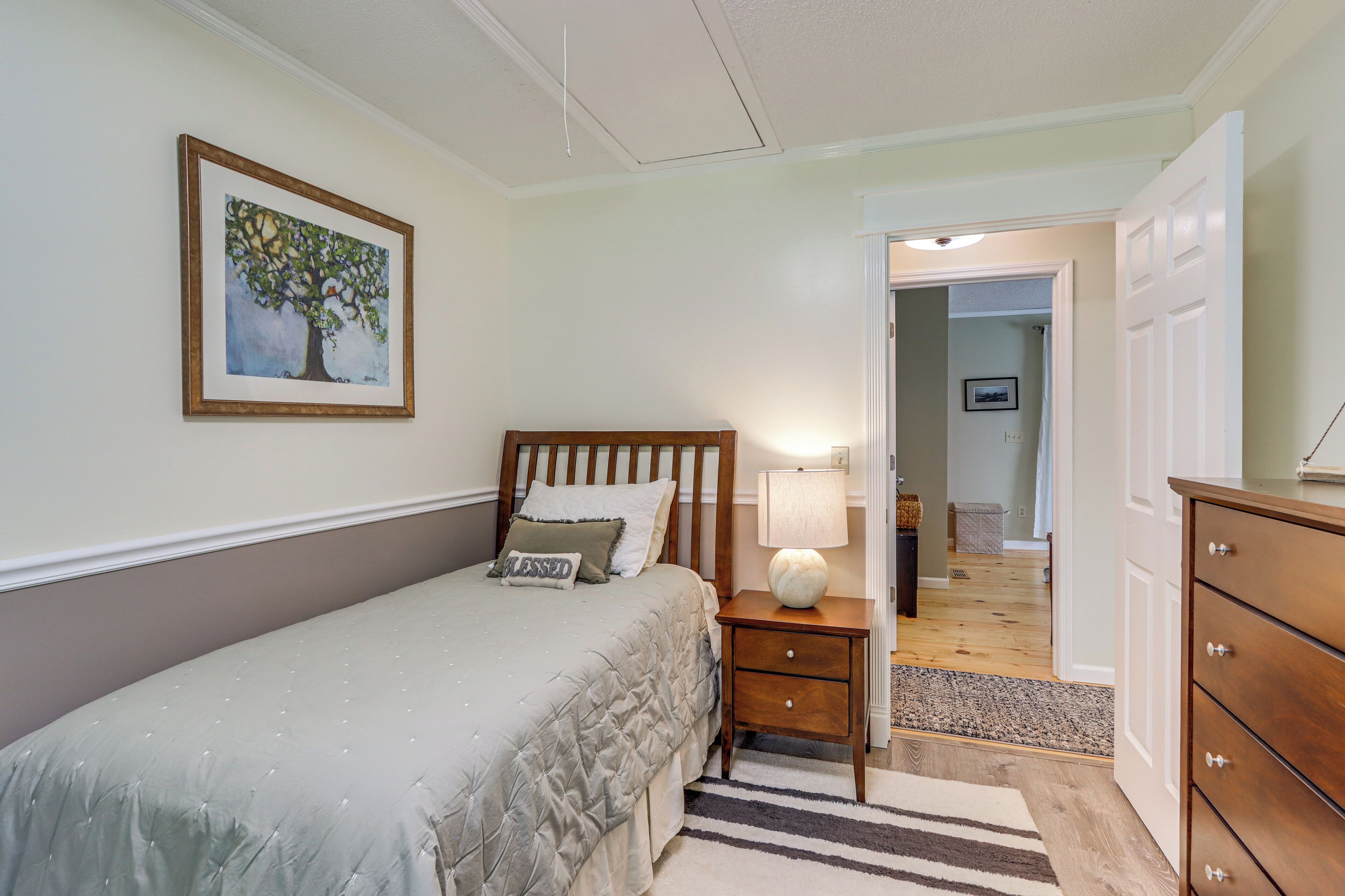 A bedroom with a bed, nightstand, dresser, and a painting on the wall.