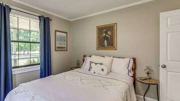 A bedroom with a bed, a nightstand, a window with curtains, a door, and a framed picture on the wall.