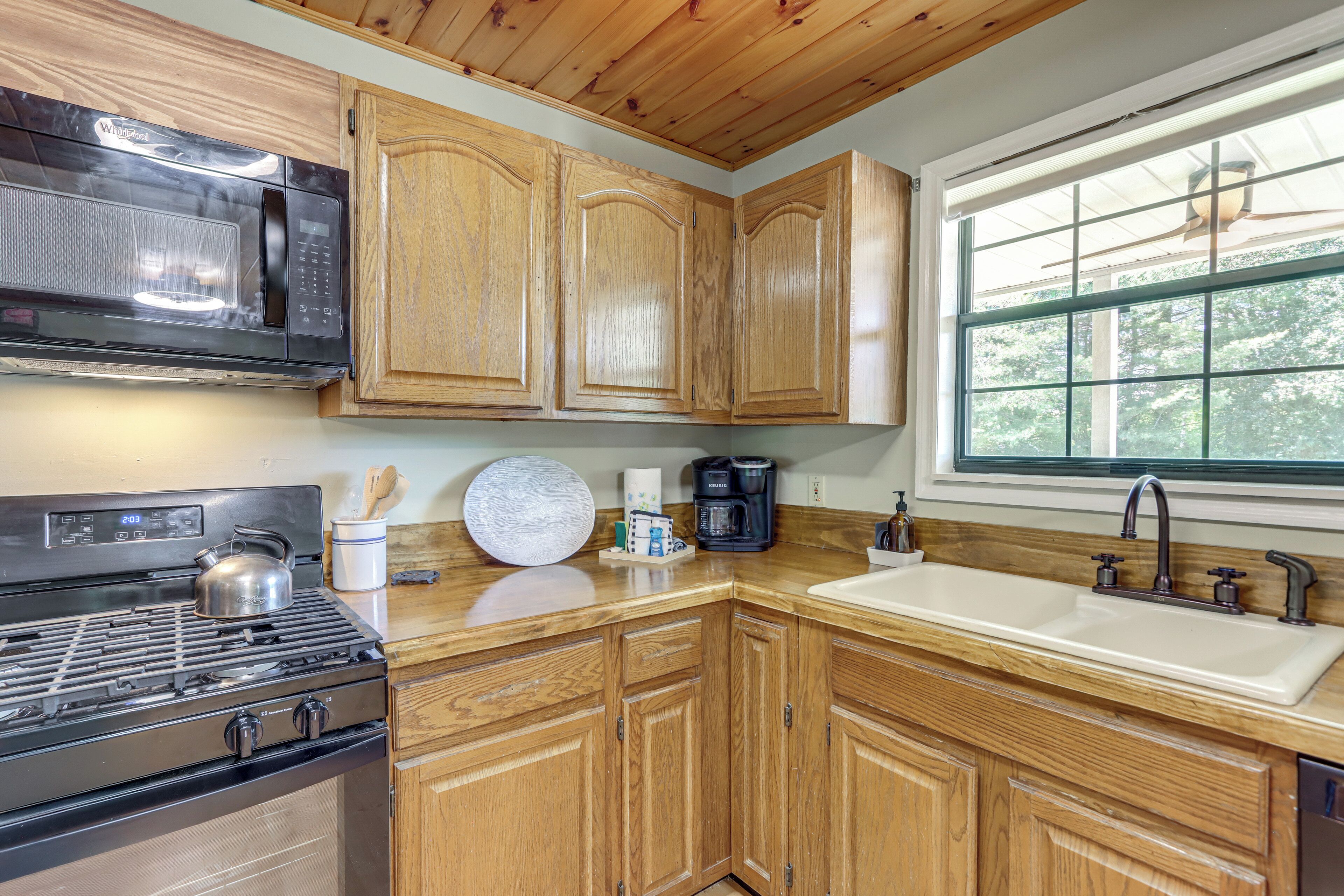 A kitchen with wooden cabinets, a microwave, a stove, a sink, and a window.