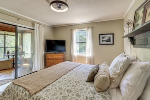 Un dormitorio con cama, televisor, cómoda y ventana con cortinas.