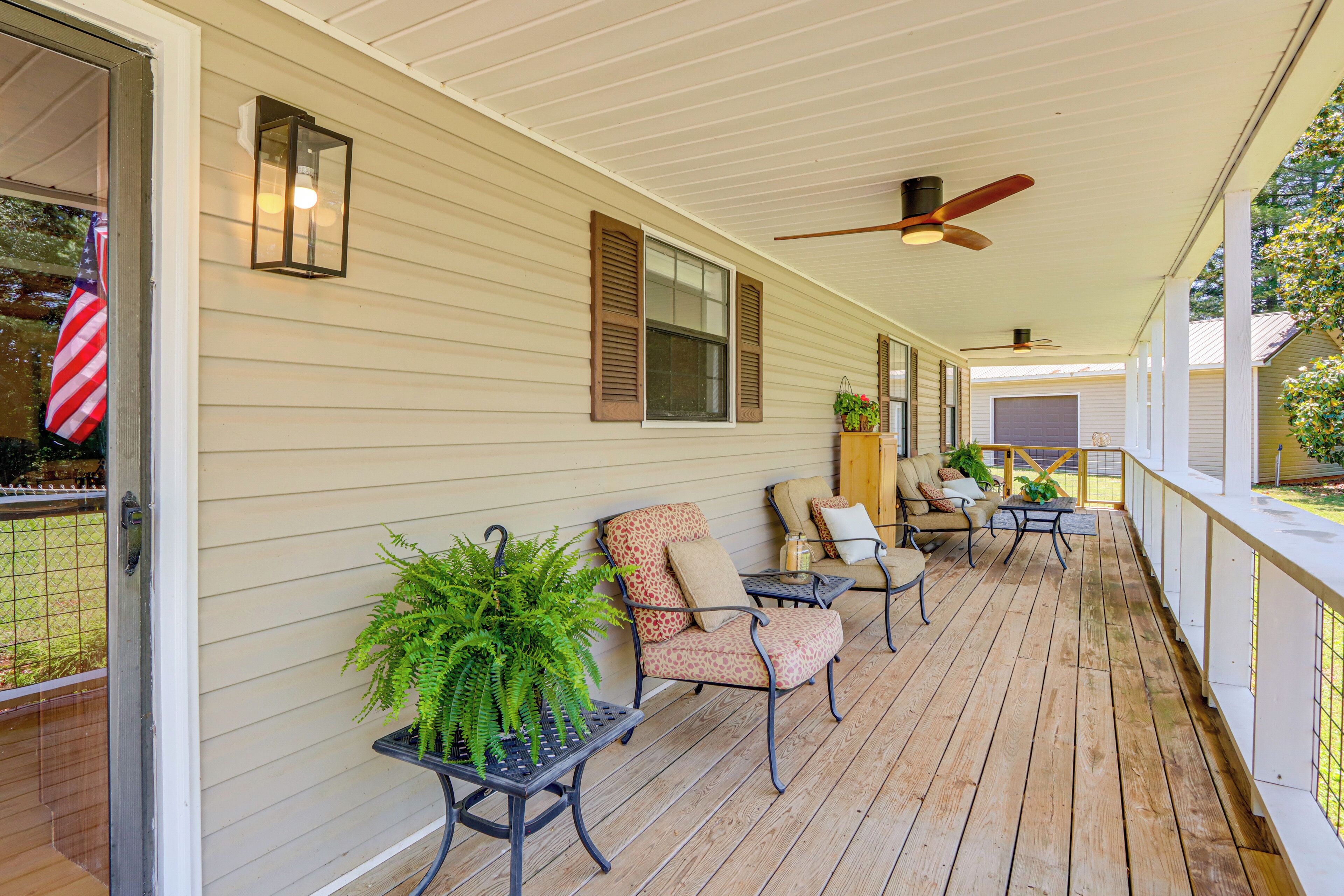 A covered porch with wooden flooring, a ceiling fan, and outdoor seating with chairs and tables.