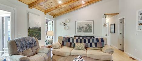Un salón con techo de madera, un sofá beige, una mesita redonda y un cuadro grande en la pared.