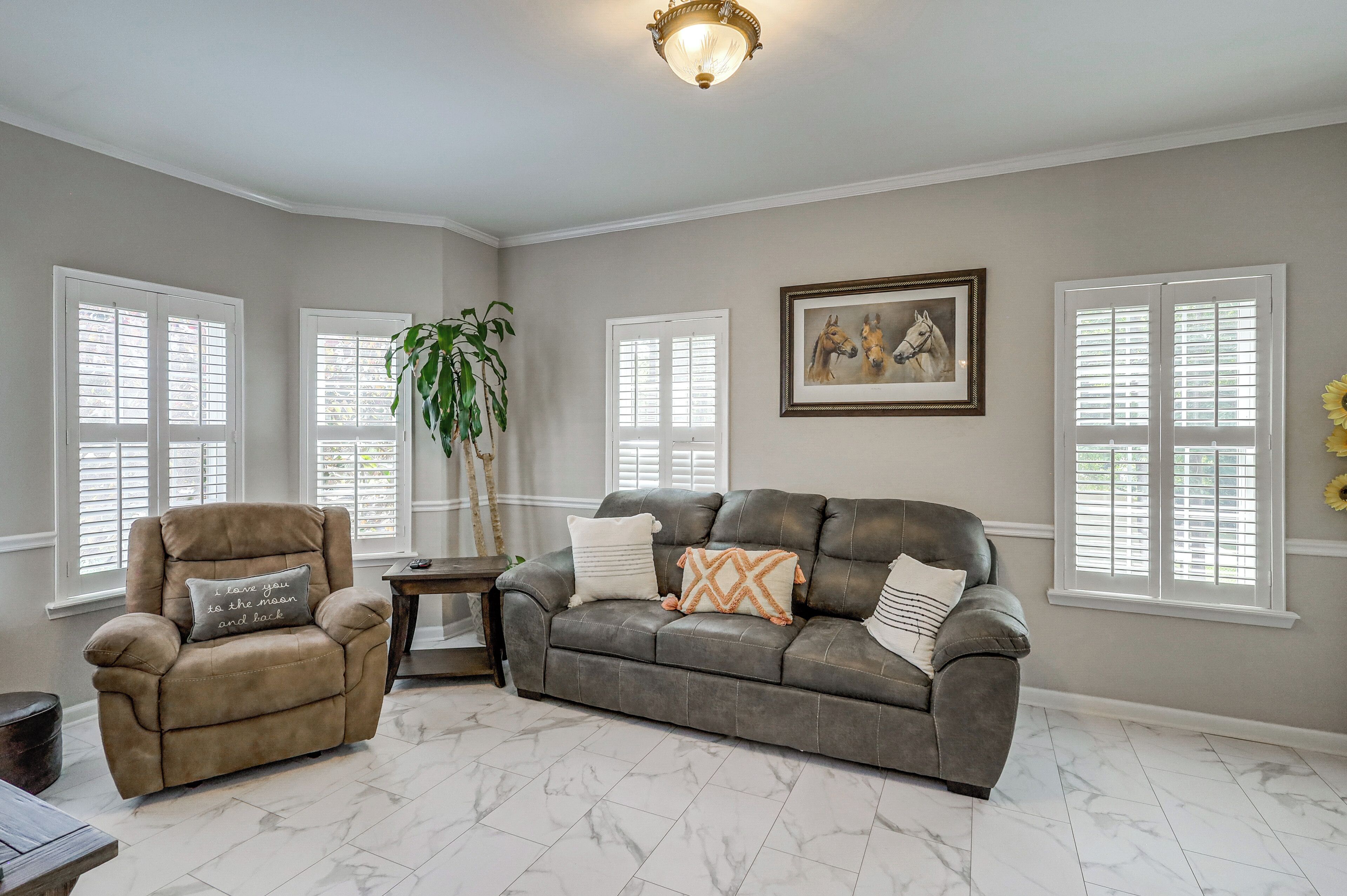 A living room with a leather sofa, a recliner, a potted plant, and a framed horse painting.