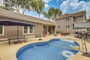 A backyard with a swimming pool, patio furniture, and a covered seating area.