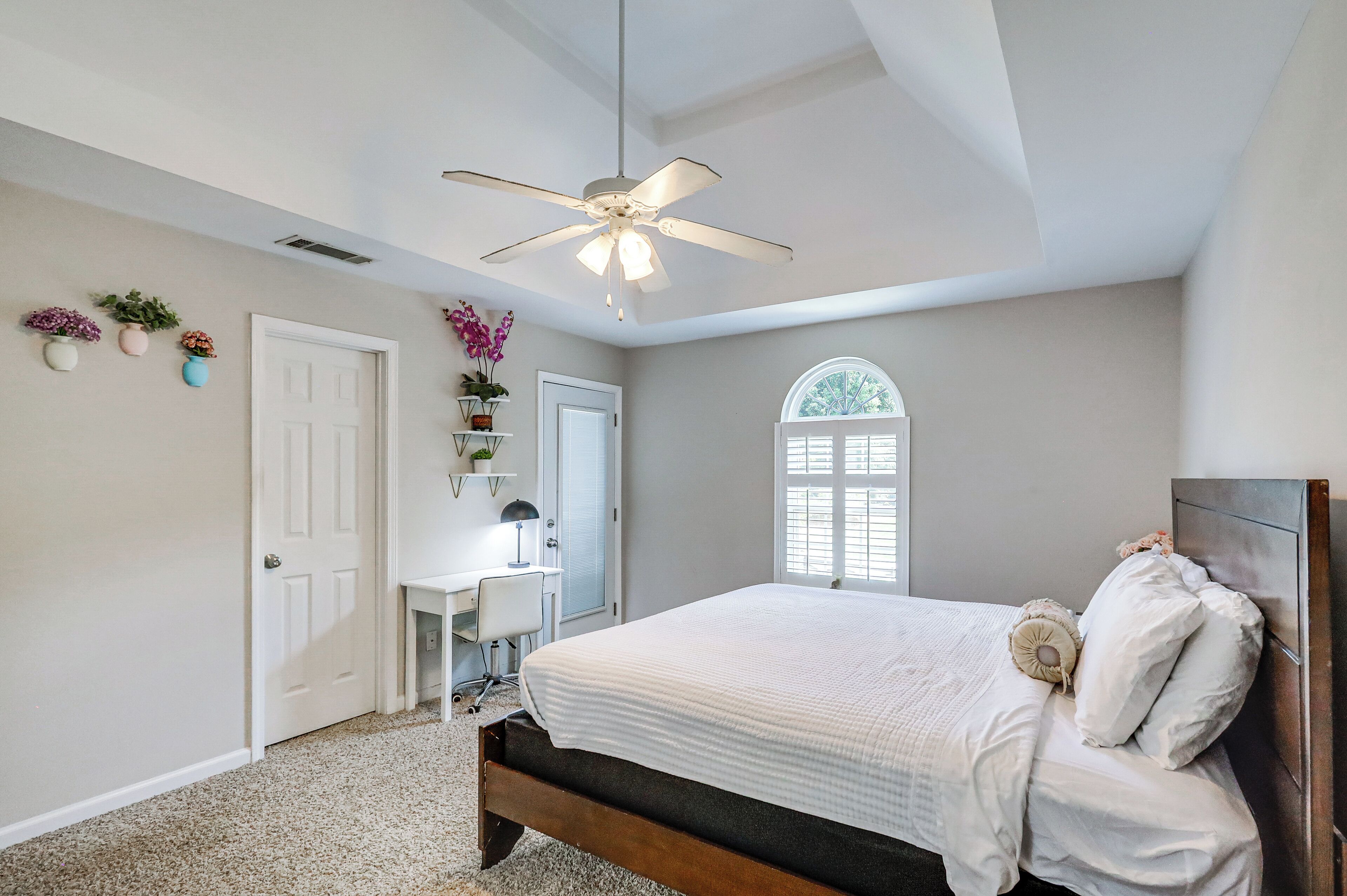 A bedroom with a bed, a desk, a chair, a ceiling fan, and a window.