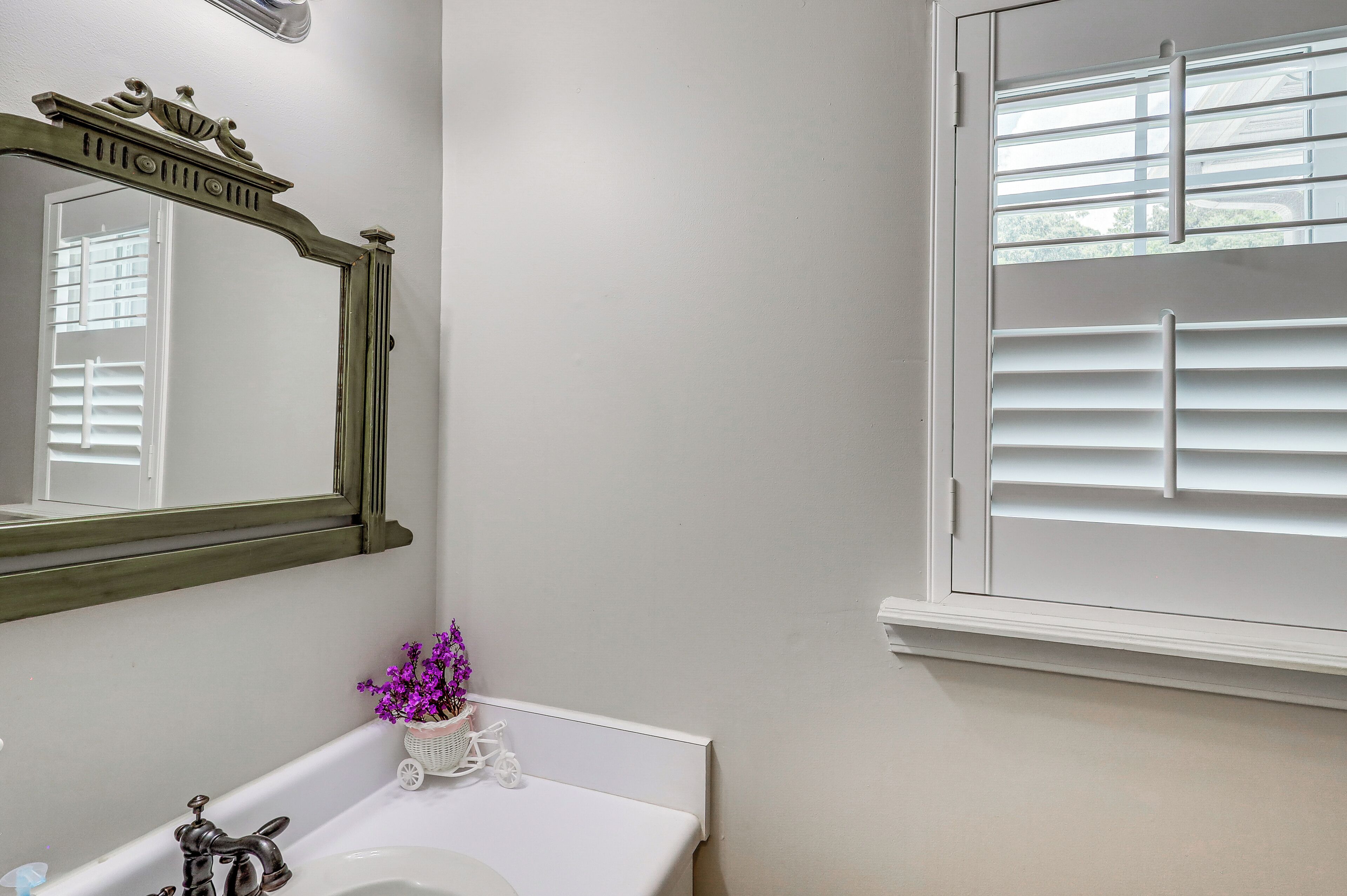 A bathroom with a white sink, a mirror with an ornate frame, and a window with blinds.